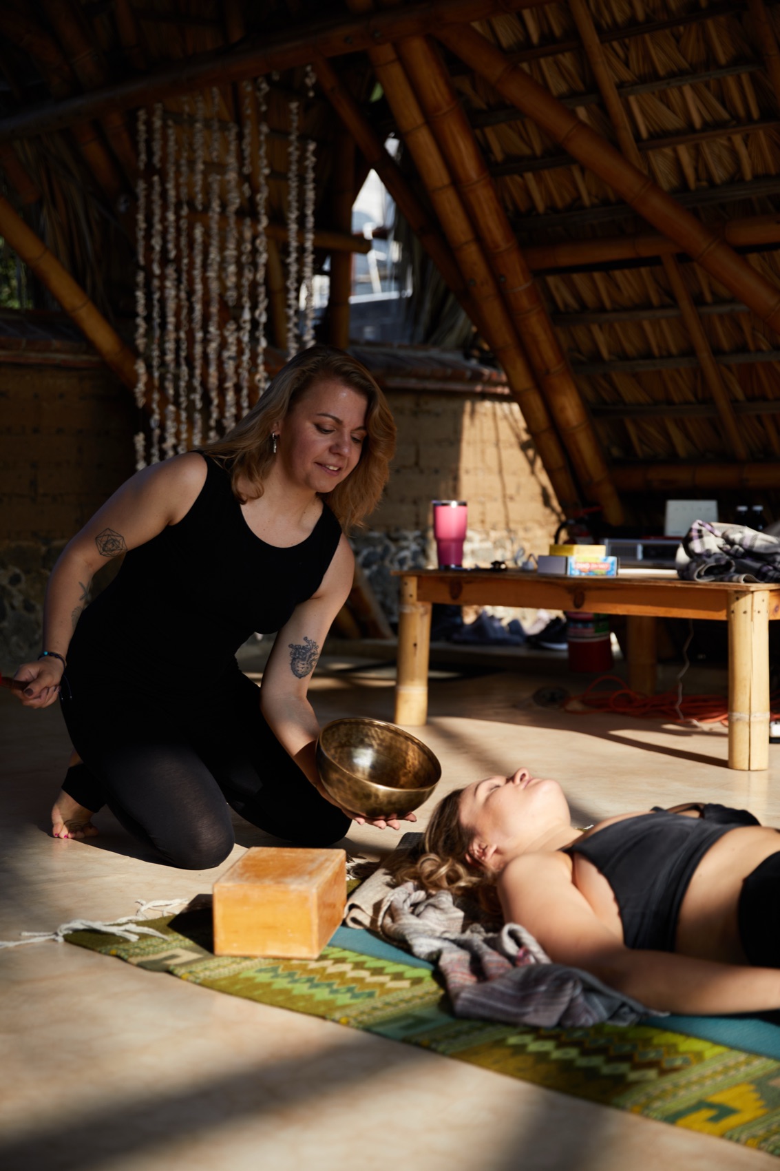 Julia guiding a client through a somatic session with a singing bowl in a palapa studio