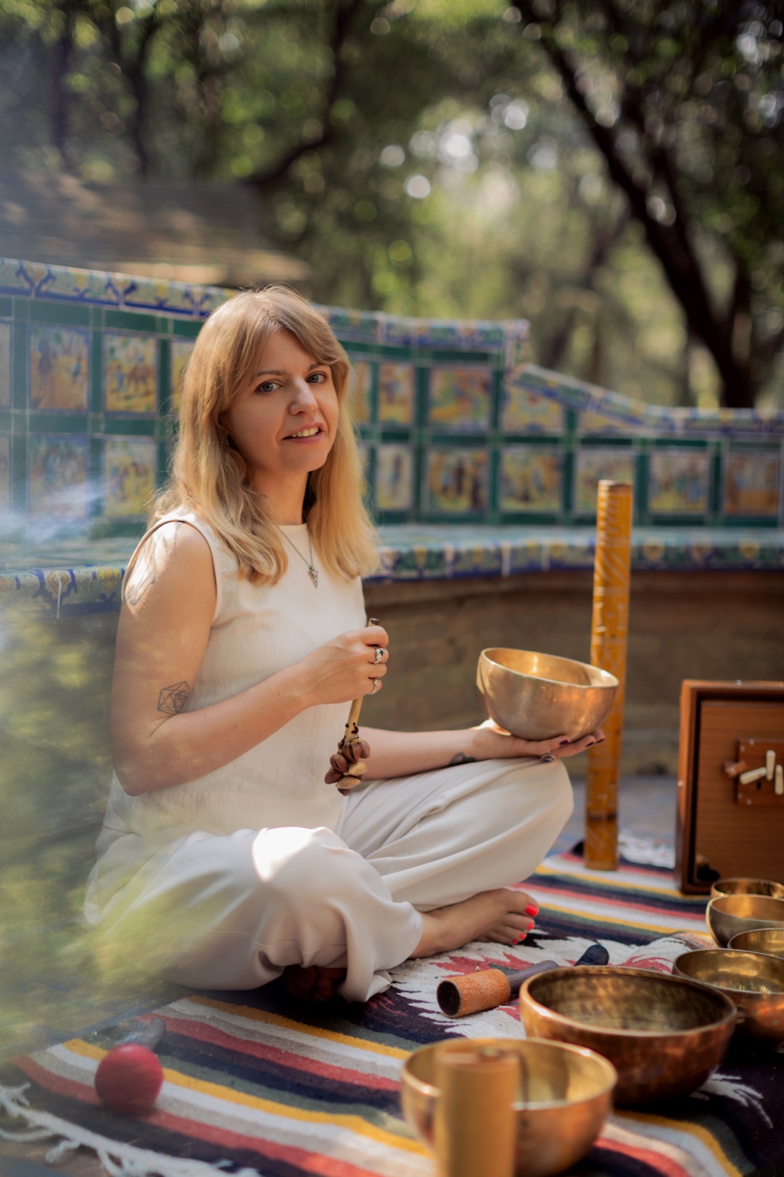 Julia Klykova seated with Tibetan singing bowls on a woven blanket in a Mexico City park